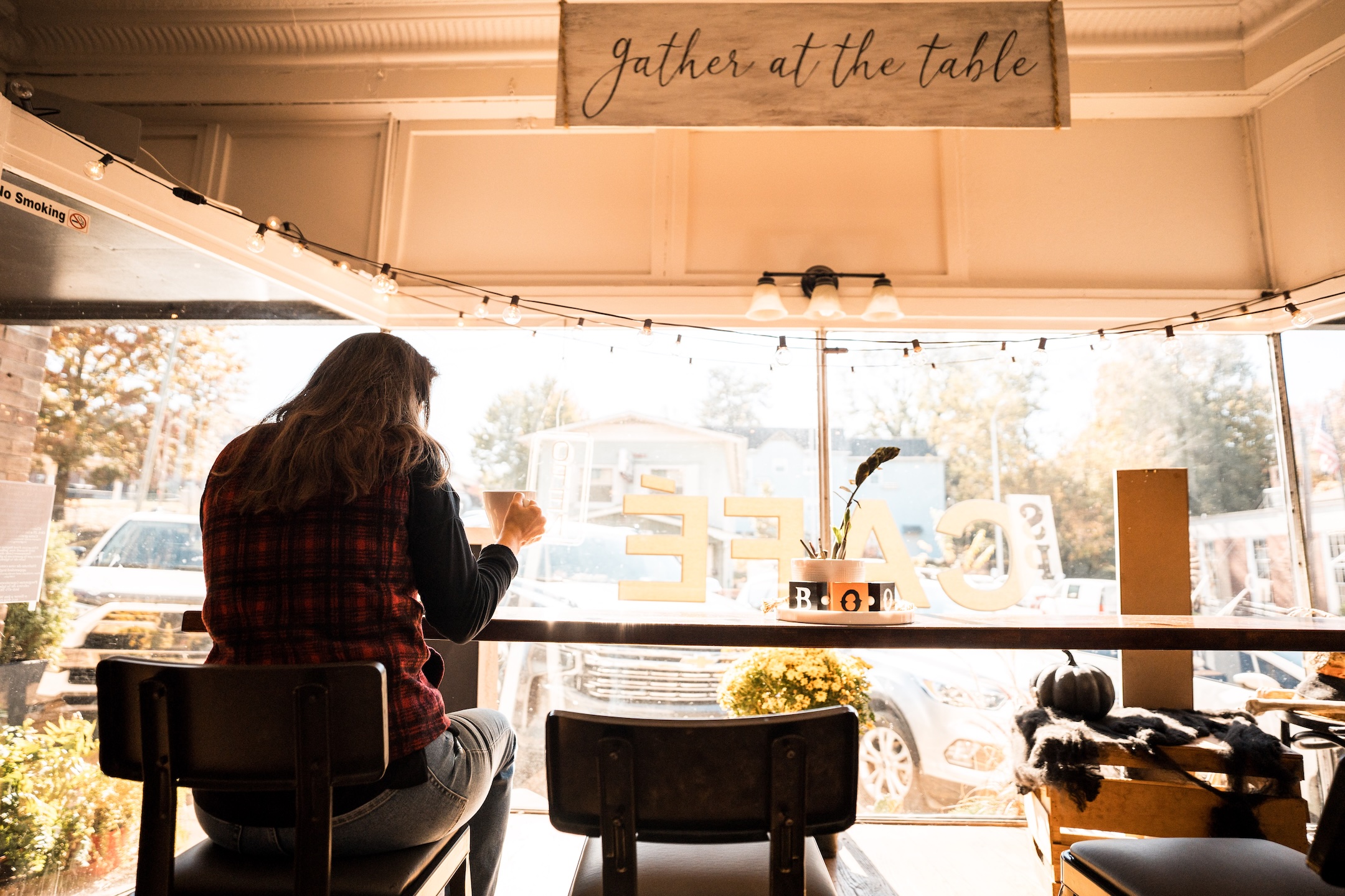 Woman sitting at cafe bar  drinking a coffee with fall scenery out the window