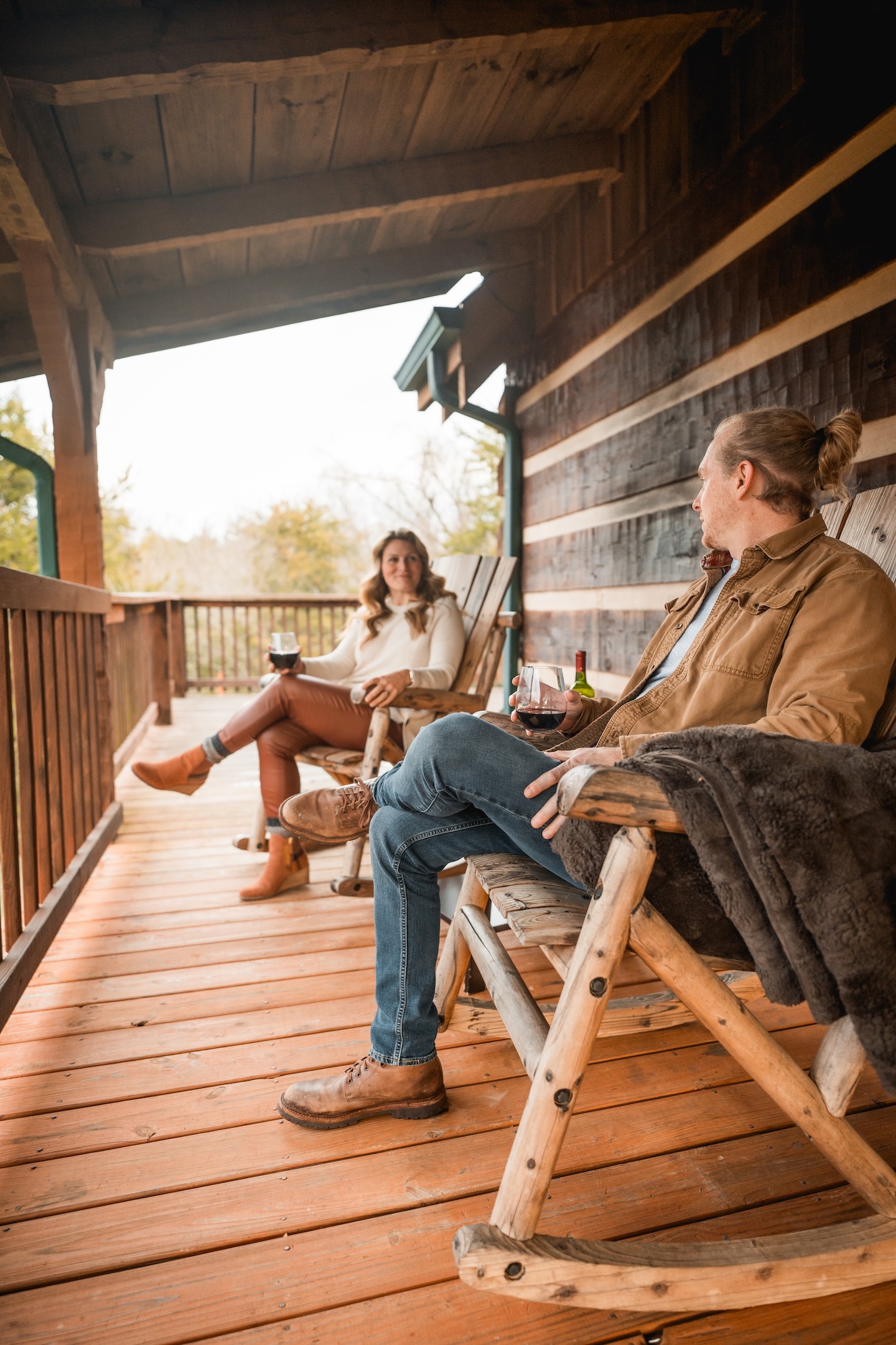 Couple sitting on porch of cabin drinking wine and laughing over a story
