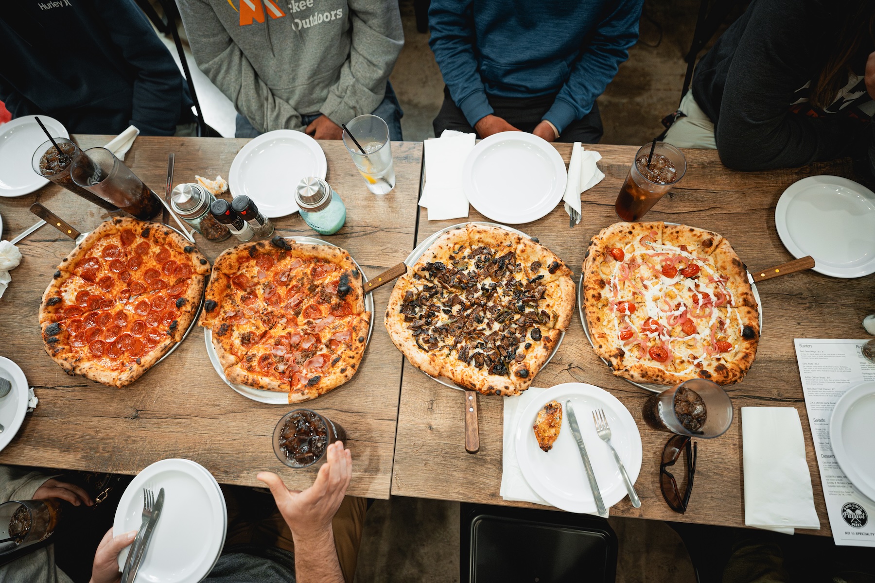 A group of friends sitting around a table with four delicious pizzas from Patriot Wood-fired Pizza