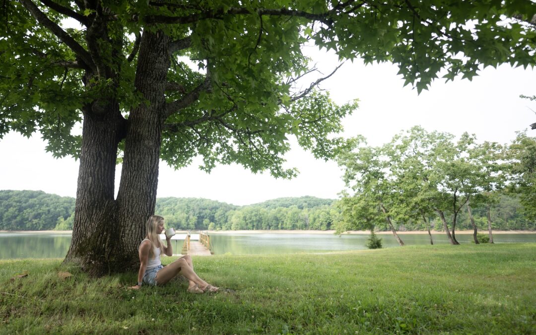 Woman sitting under a large maple tree, enjoying a cup of coffee with Douglas Lake in the Background.